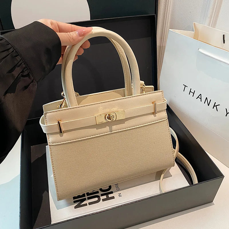 Sac à main beige élégant avec poignées et fermoir doré, présenté dans une boîte