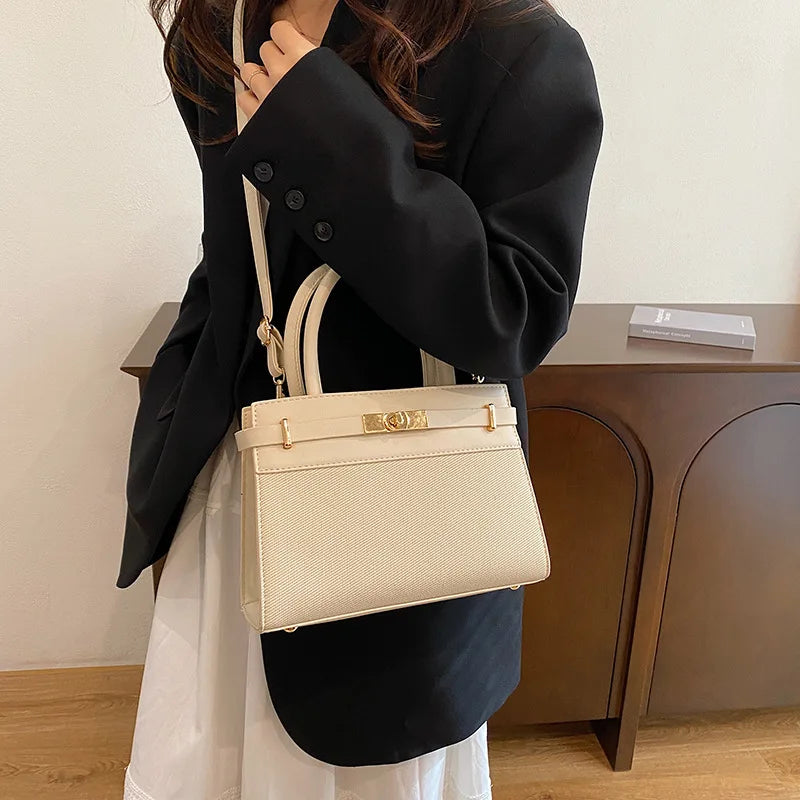 Sac à main beige élégant avec fermeture dorée, porté par une femme en blazer noir