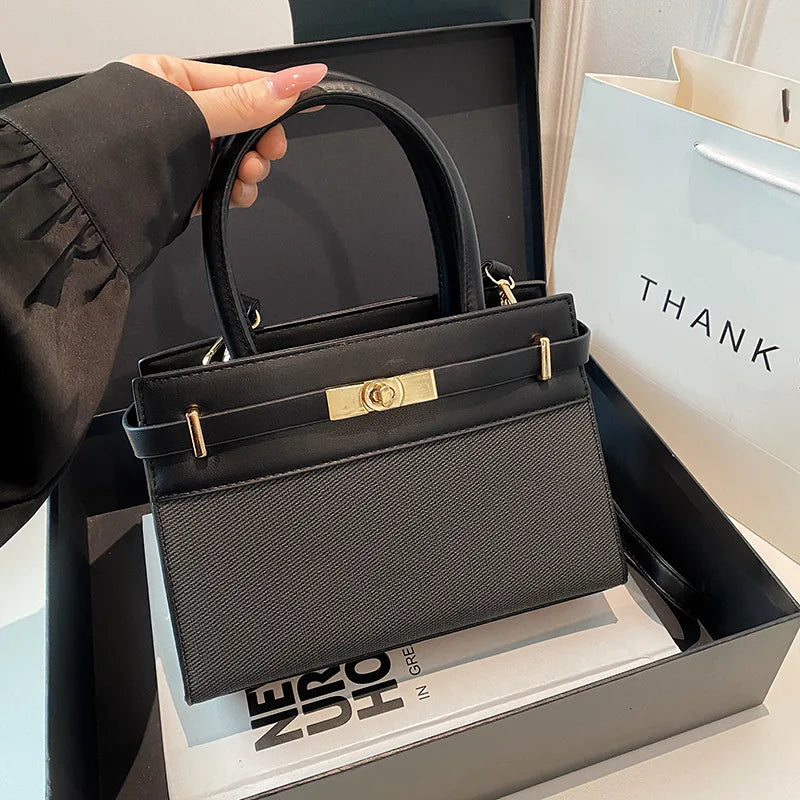Sac à main noir élégant avec fermoir doré, idéal pour femme, présenté dans son emballage cadeau